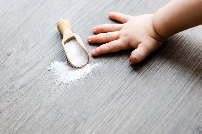 white salt in brown wooden spoon on the table or old floor with child hand