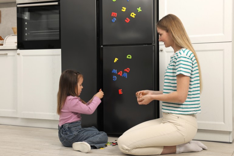 Mom and daughter putting magnetic letters on fridge at home. Learning alphabet