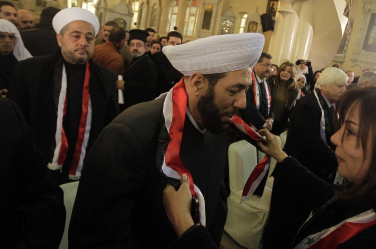 A Syrian woman presents a national flag to Syria's Grand Mufti Ahmad Badreddin Hassoun during a mass held at a Greek Orthodox church in Damascus on January 9, 2012 in memory of two victims of recent fighting in the country, his son who was killed in October in Homs, and a Christian boy, killed recently in the central flashpoint city. The Arab League pressed on with its mission to halt 10 months of bloodshed in Syria despite charges it was only serving to cover up the regime's deadly crackdown on protests. AFP HOTO/JOSEPH EID (Photo by JOSEPH EID / AFP)