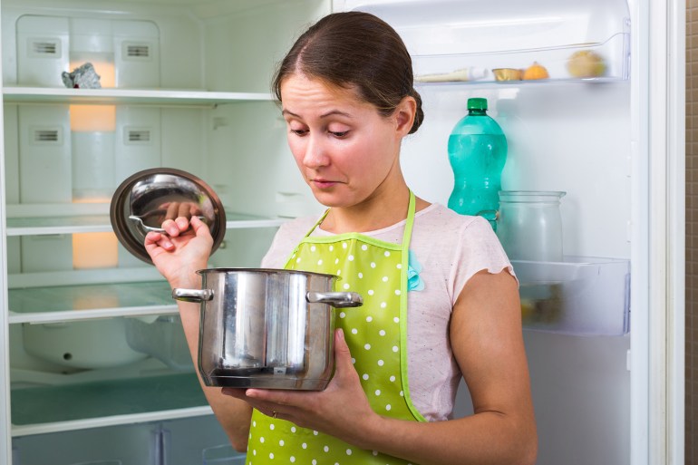 Hungry upset young woman in apron standing near fridge with empty shelves ; Shutterstock ID 695089225; purchase_order: aj; job: ; client: ; other: