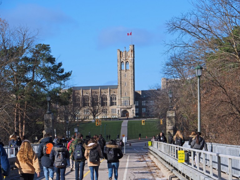 LONDON, ONTARIO, CANADA - DECEMBER 2018: Students cross a bridge on their way to the campus of the University of Western Ontario, with the gothic tower of University College in the background.