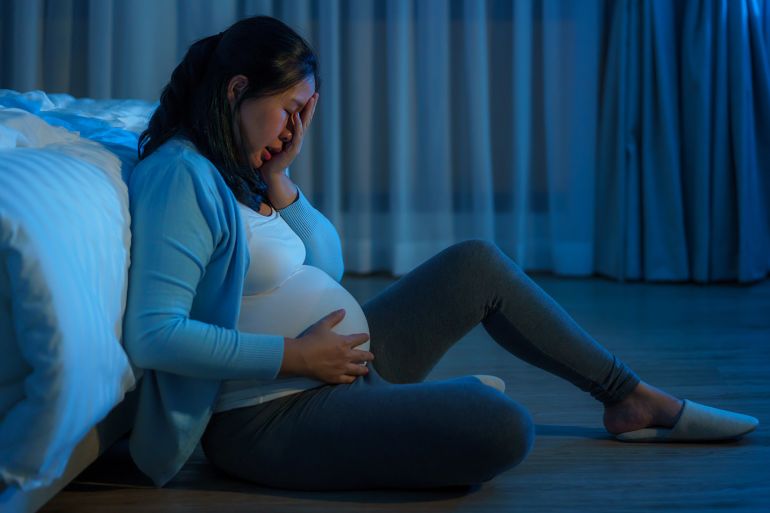 Amid her pregnancy journey, an Asian woman experiences sadness, tears flowing as emotions overwhelm her, seeking solace on her home bed.
