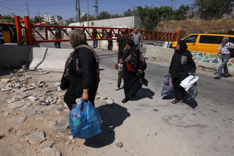 Palestinians carrying their belongings move on foot as closed iron gates set up by Israeli forces prevent vehicle movement after Israeli authorities closed off all entrance and exist roads of Hebron city in the occupied West Bank on June 14, 2025. (Photo by HAZEM BADER / AFP)