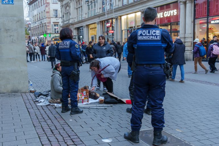 Strasbourg, France; December 28, 2024: Municipal police officers and local citizens engaging with a homeless woman sitting on the street with her belongings and dog