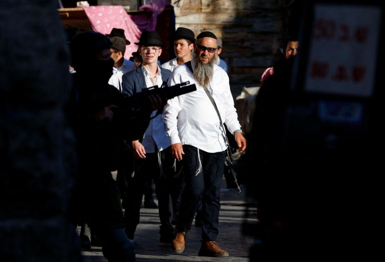 Settlers look on as Israeli troops stand guard during a weekly settlers' tour in Hebron, in the Israeli-occupied West Bank July 19, 2025. REUTERS/Mussa Qawasma
