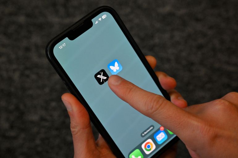 This illustration photograph taken in Brussels on November 18, 2024, shows the logos of US social network X (former Twitter) (L) and Bluesky displayed on a mobile phone. - The bluesky social network has soared to one of the top positions in social network downloads in app stores since the US election and establishes as an alternative to X. (Photo by Nicolas TUCAT / AFP)